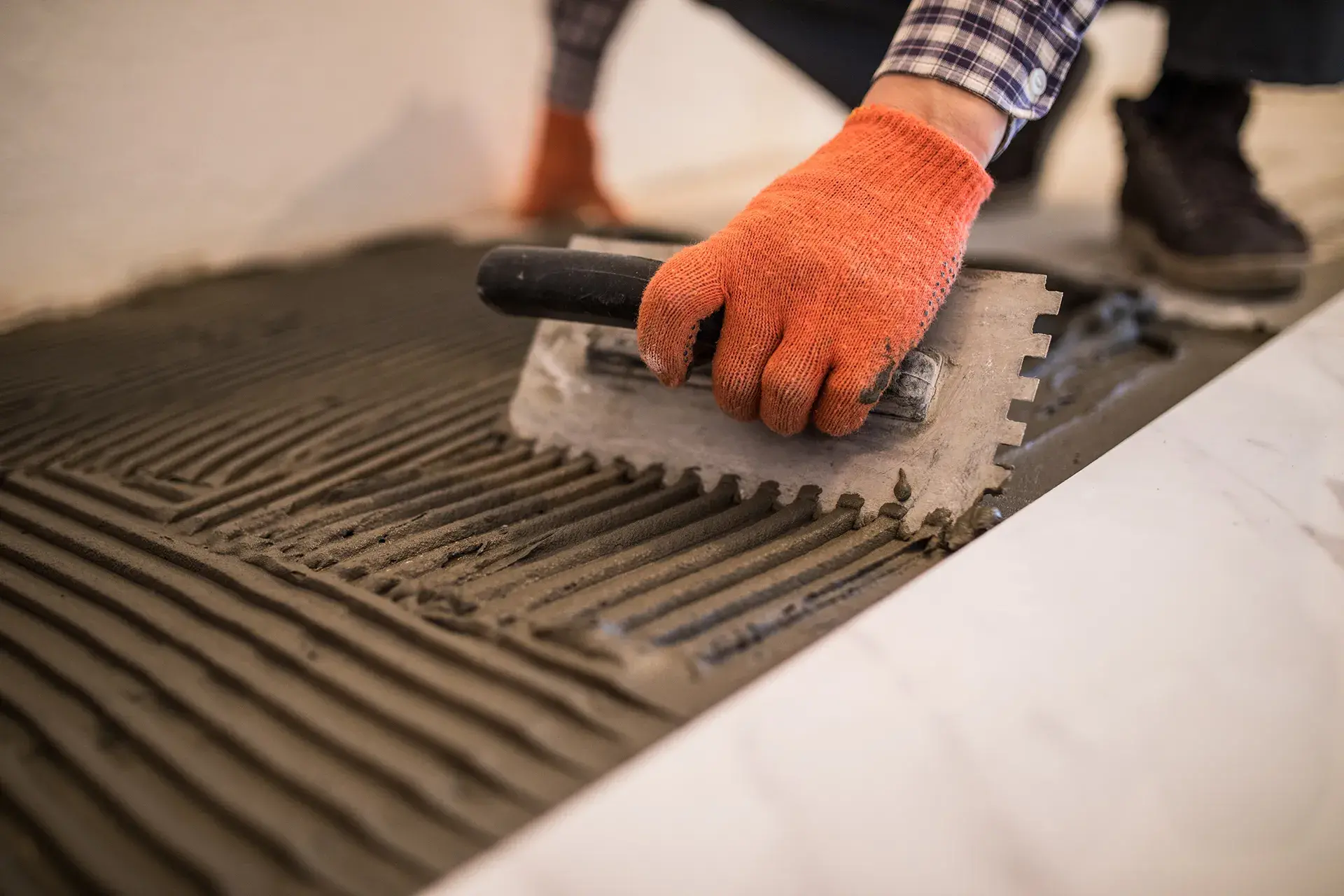 laying-ceramic-tiles-troweling-mortar-onto-concrete-floor-in-preparation-for-laying-white-floor-tile AdobeStock_216691740